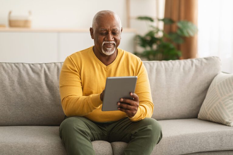 Homme noir senior utilisant une tablette pour naviguer sur Internet assis à la maison